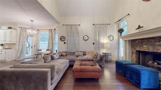 living room with dark hardwood / wood-style flooring, an inviting chandelier, and a stone fireplace