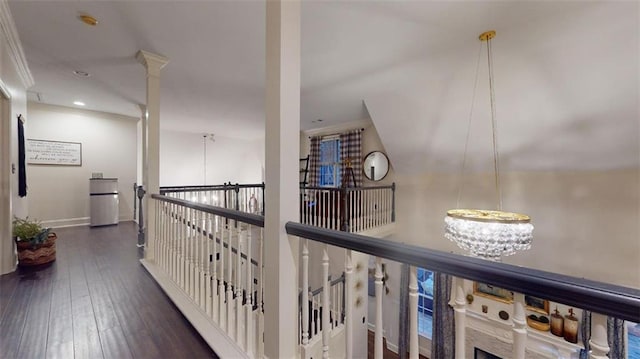 corridor featuring ornamental molding, ornate columns, an inviting chandelier, and dark wood-type flooring