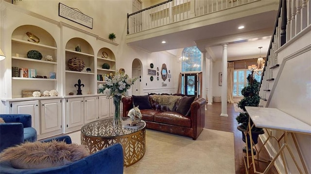 living room with a notable chandelier, built in shelves, light hardwood / wood-style floors, ornate columns, and ornamental molding