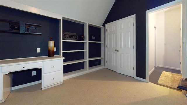 unfurnished office with built in desk, vaulted ceiling, and light colored carpet