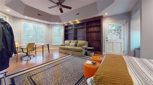 bedroom with ceiling fan, hardwood / wood-style floors, and a tray ceiling