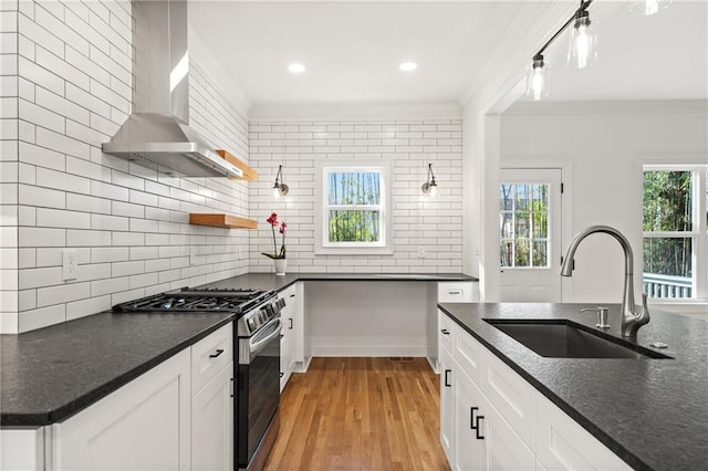 kitchen featuring wall chimney exhaust hood, ornamental molding, a sink, stainless steel range with gas cooktop, and backsplash