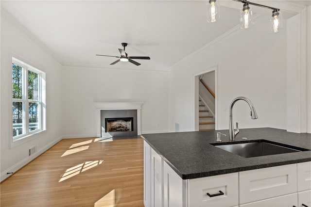 kitchen with light wood finished floors, white cabinets, a fireplace with flush hearth, ornamental molding, and a sink