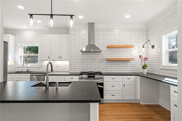 kitchen with dark countertops, wall chimney range hood, stainless steel appliances, and a sink