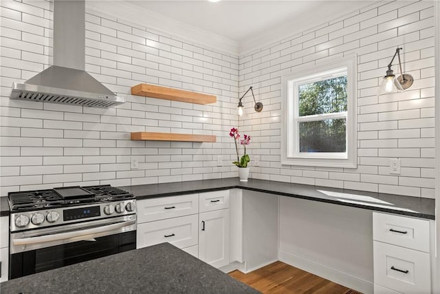 kitchen featuring tasteful backsplash, ornamental molding, white cabinets, stainless steel gas range oven, and wall chimney exhaust hood