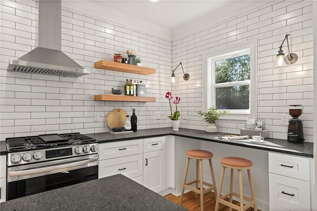 kitchen featuring dark countertops, wall chimney exhaust hood, stainless steel gas range oven, and ornamental molding