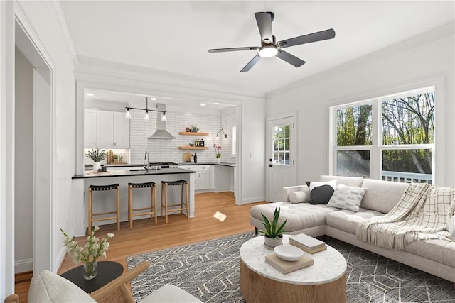 living area featuring light wood finished floors, baseboards, a ceiling fan, and crown molding