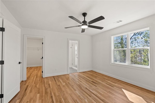 unfurnished bedroom featuring light wood finished floors, visible vents, baseboards, a ceiling fan, and a spacious closet