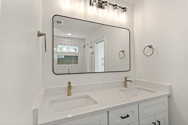 bathroom featuring a tile shower, double vanity, a sink, and visible vents