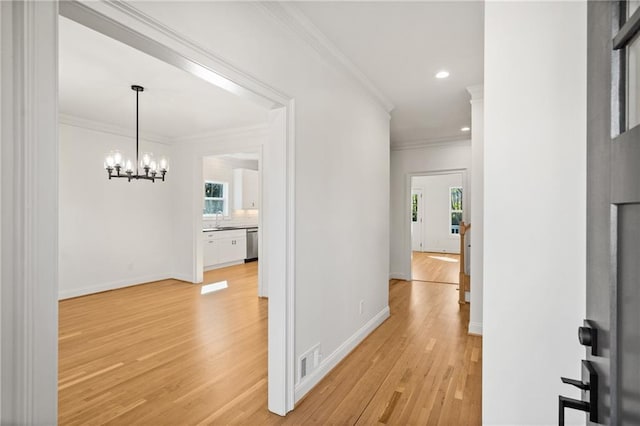 hallway with a notable chandelier, light wood finished floors, visible vents, ornamental molding, and baseboards