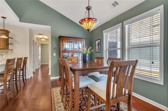 dining room with arched walkways, visible vents, lofted ceiling, and wood finished floors