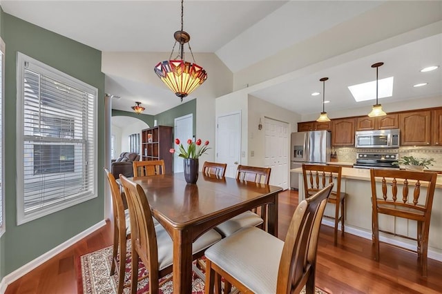 dining space featuring baseboards, vaulted ceiling with skylight, recessed lighting, arched walkways, and dark wood-type flooring