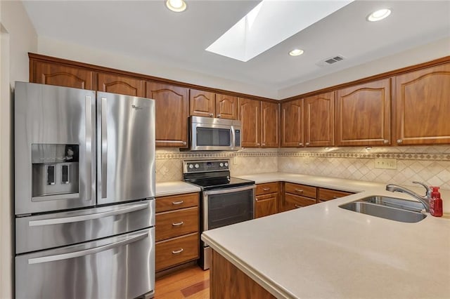 kitchen with light countertops, a skylight, appliances with stainless steel finishes, and a sink