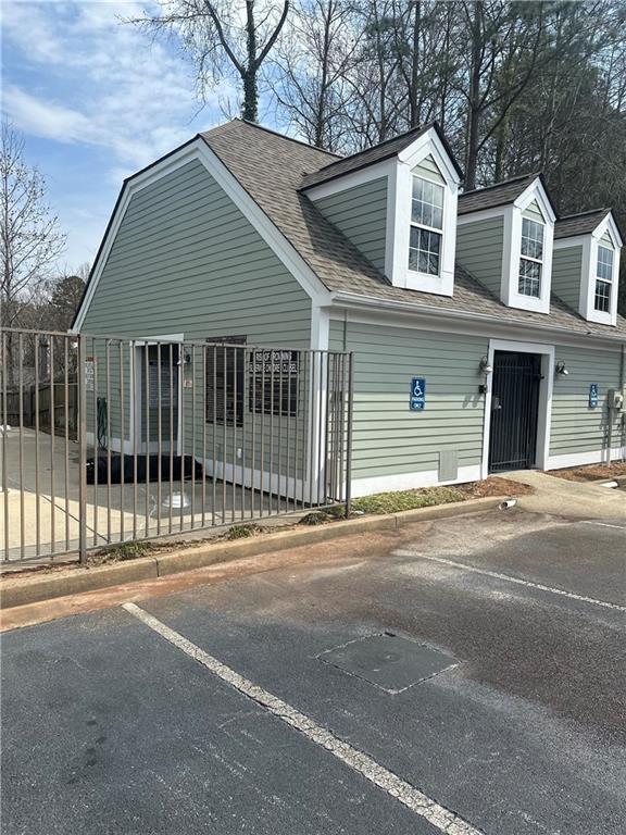 view of front of house with fence, roof with shingles, and uncovered parking