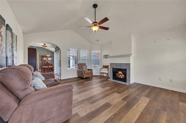 living room with vaulted ceiling, a tile fireplace, wood finished floors, arched walkways, and a ceiling fan