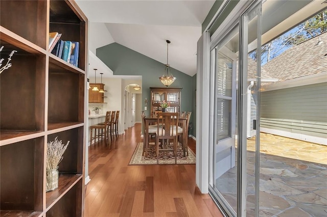 dining space featuring arched walkways, plenty of natural light, lofted ceiling, and wood finished floors