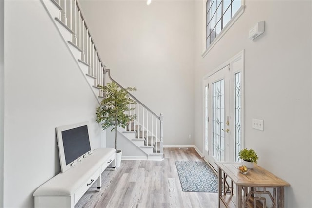 entrance foyer featuring french doors, stairway, a towering ceiling, light wood-style floors, and baseboards