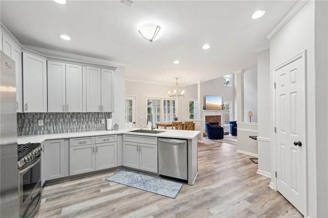 kitchen with stainless steel appliances, light countertops, hanging light fixtures, a sink, and a peninsula