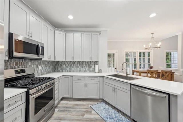 kitchen featuring backsplash, hanging light fixtures, stainless steel appliances, light countertops, and a sink