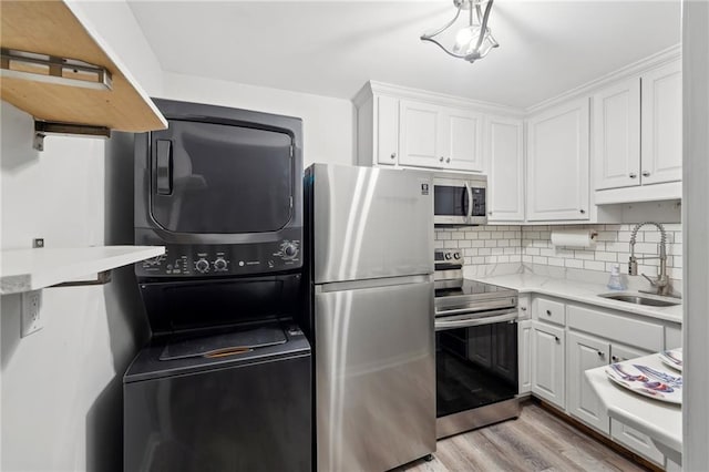 kitchen with white cabinetry, stainless steel appliances, a sink, and stacked washer and clothes dryer