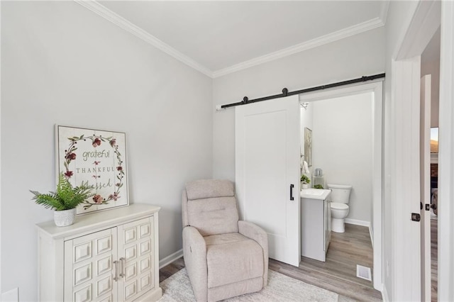 living area with ornamental molding, a barn door, light wood-type flooring, and baseboards