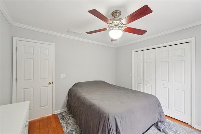 bedroom with a closet, visible vents, ornamental molding, ceiling fan, and wood finished floors