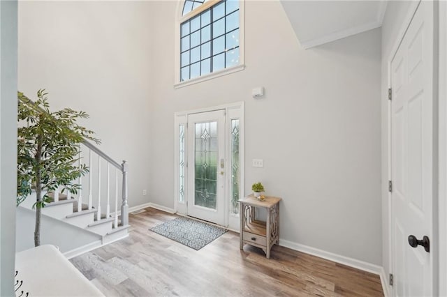 entryway with light wood finished floors, stairway, a high ceiling, ornamental molding, and baseboards