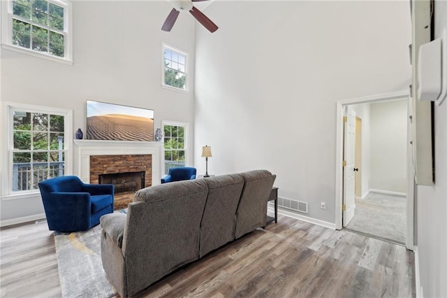 living room with light wood finished floors, a stone fireplace, a towering ceiling, and baseboards