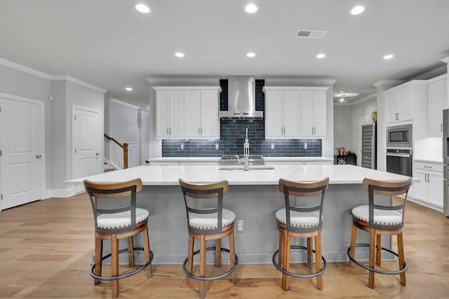 kitchen with visible vents, light wood-style flooring, stainless steel microwave, a spacious island, and wall chimney exhaust hood