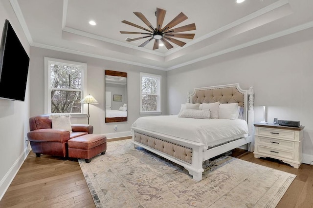 bedroom with baseboards, crown molding, a tray ceiling, and hardwood / wood-style floors