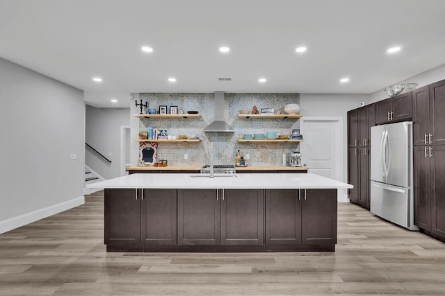 kitchen featuring light countertops, freestanding refrigerator, wall chimney range hood, and open shelves