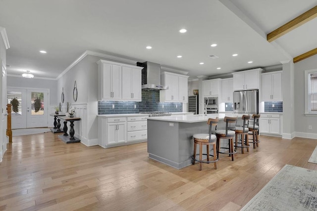 kitchen with a kitchen bar, wall chimney range hood, stainless steel appliances, french doors, and light wood finished floors