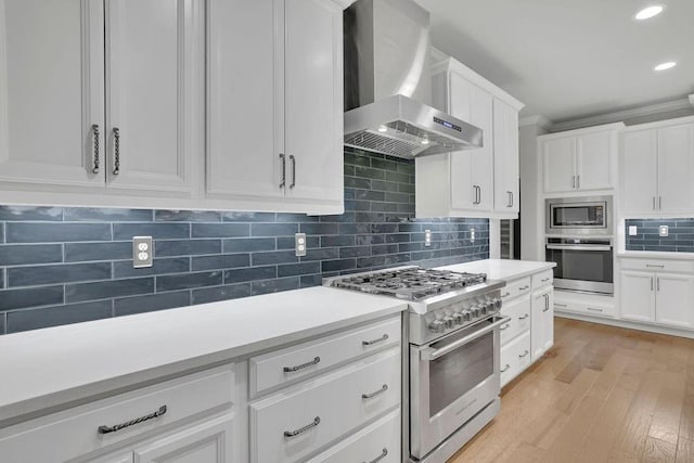 kitchen with stainless steel appliances, light countertops, decorative backsplash, and wall chimney range hood
