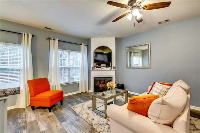 living area featuring a glass covered fireplace, visible vents, baseboards, and wood finished floors