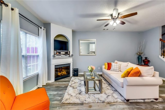 living room featuring baseboards, visible vents, wood finished floors, and a glass covered fireplace