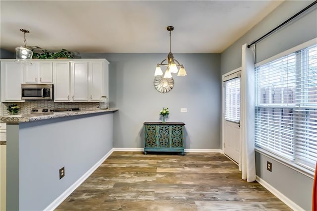 kitchen featuring wood finished floors, white cabinetry, light countertops, stainless steel microwave, and pendant lighting