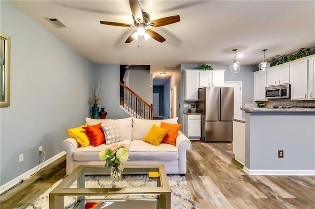 living area with light wood-style flooring, stairs, visible vents, and baseboards