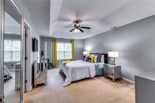 bedroom featuring a raised ceiling, light carpet, visible vents, and baseboards