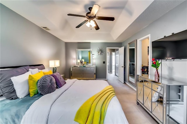 bedroom featuring ceiling fan, a raised ceiling, visible vents, and light colored carpet