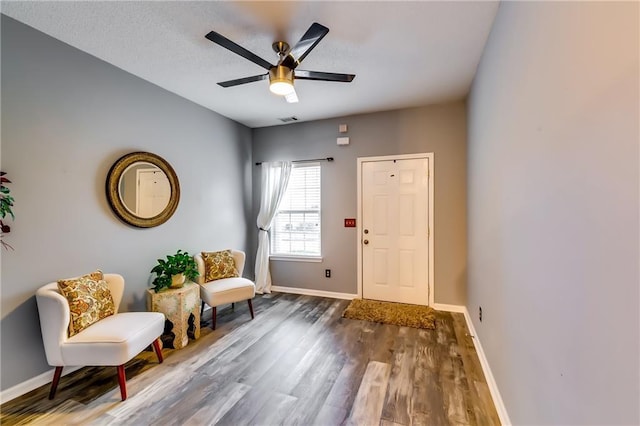 living area featuring a ceiling fan, visible vents, baseboards, and wood finished floors