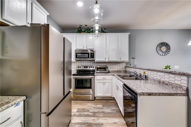 kitchen featuring stainless steel appliances, white cabinetry, a sink, and decorative light fixtures