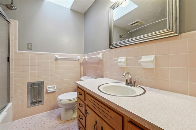 full bathroom featuring tile patterned flooring, vanity, bath / shower combo with glass door, tile walls, and toilet