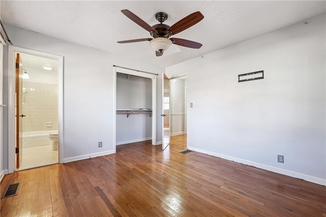 unfurnished bedroom with ceiling fan, dark wood-type flooring, a closet, and ensuite bath