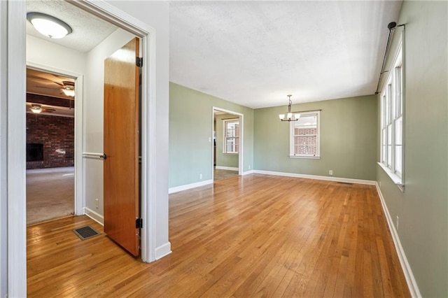 spare room with a brick fireplace, a chandelier, and light hardwood / wood-style floors