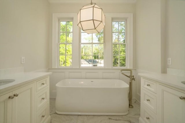 full bath featuring two vanities, plenty of natural light, a freestanding tub, and ornamental molding