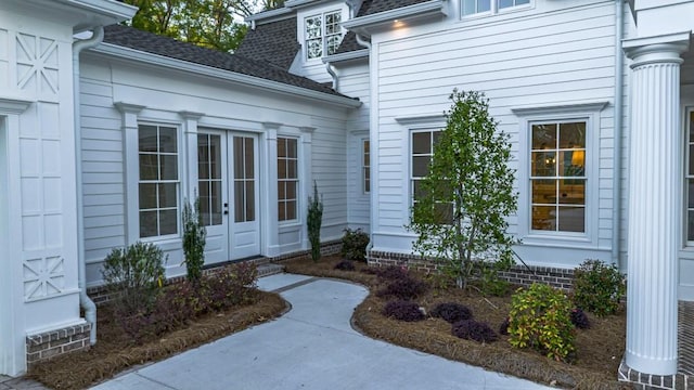 view of exterior entry featuring french doors and a shingled roof