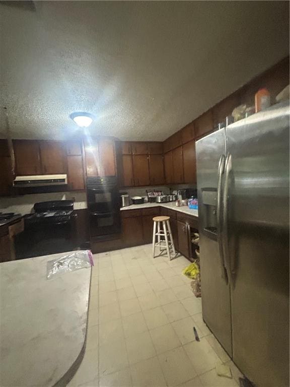 kitchen with stainless steel fridge, black double oven, and a textured ceiling