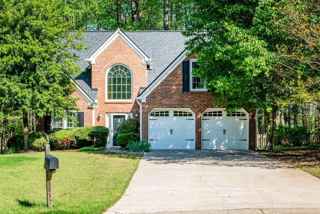 traditional-style house with a garage, roof with shingles, a front lawn, brick siding, and concrete driveway