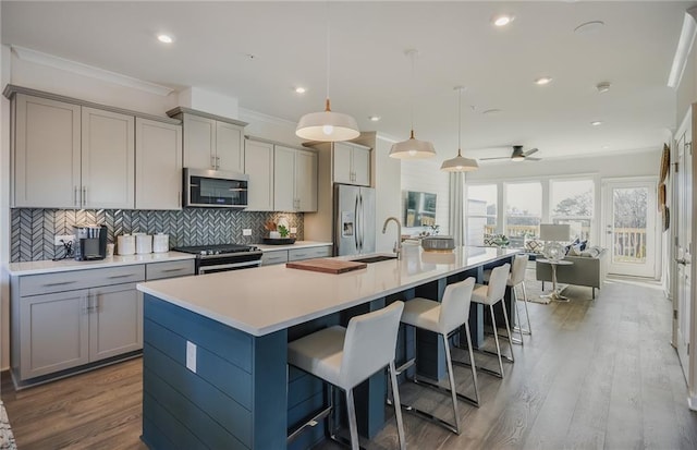 kitchen featuring a kitchen bar, a kitchen island with sink, pendant lighting, and appliances with stainless steel finishes