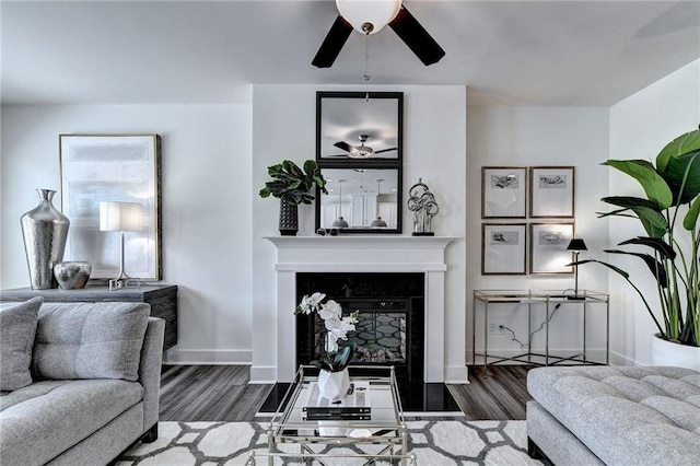 living room with a ceiling fan, a fireplace, baseboards, and wood finished floors